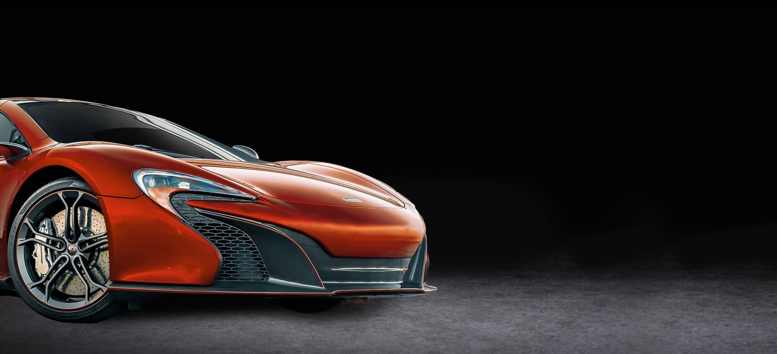 Burnt-orange McLaren lit against a black studio backdrop at Carisma Customs